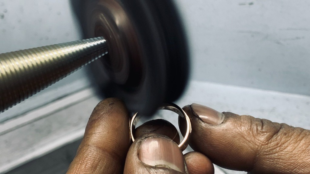Master goldsmith polishing solid gold ring band on high-speed felt lathe wheel